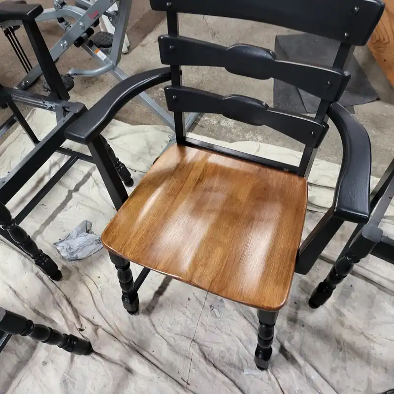 Black ladder-back chair with a refinished natural wood seat standing on drop cloths