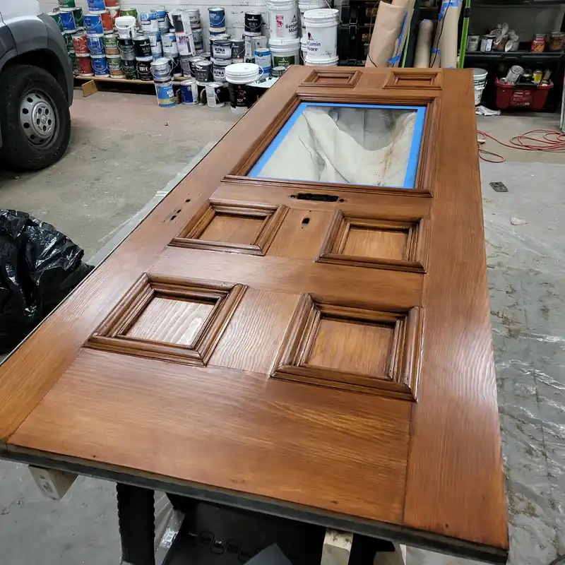 Mahogany-stained panelled door drying on a bench in the Cloudland shop, shelves of paint behind