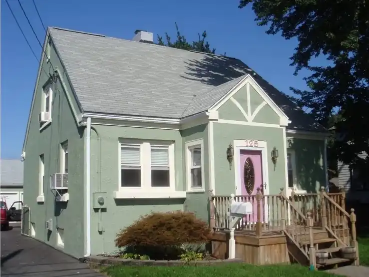 The same Cape repainted sage green with white trim and a pink front door