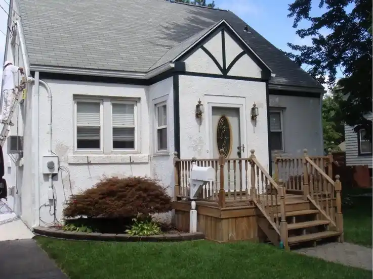 White Cape with Tudor-style trim and a stained porch before repainting