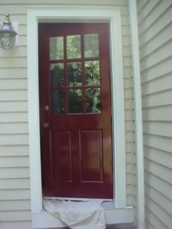 Red panelled front door with nine glass lites set in pale siding