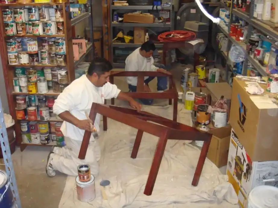 Painter refinishing a chair frame in the Cloudland shop with shelves of paint behind