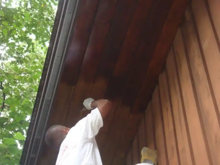 Painter staining a cedar soffit on a ladder